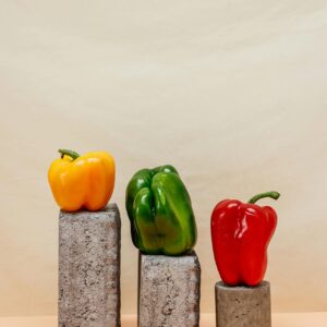 Three vibrant bell peppers placed atop concrete blocks on a neutral background.